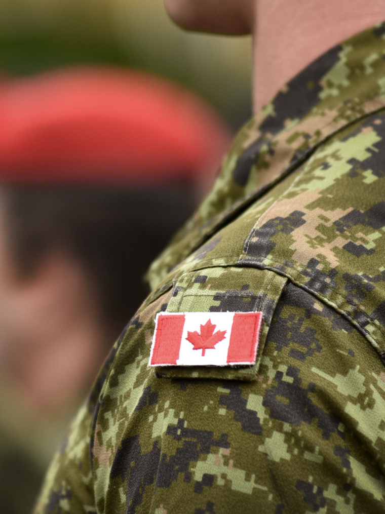A person wearing a camouflage military uniform with a Canadian flag patch on the shoulder